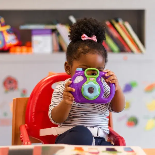 A young child holding a colourful toy camera in a classroom